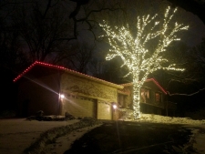 Lit up tree outside of house with red lights outlining roofChristmas Lighting Eastern Minnesota